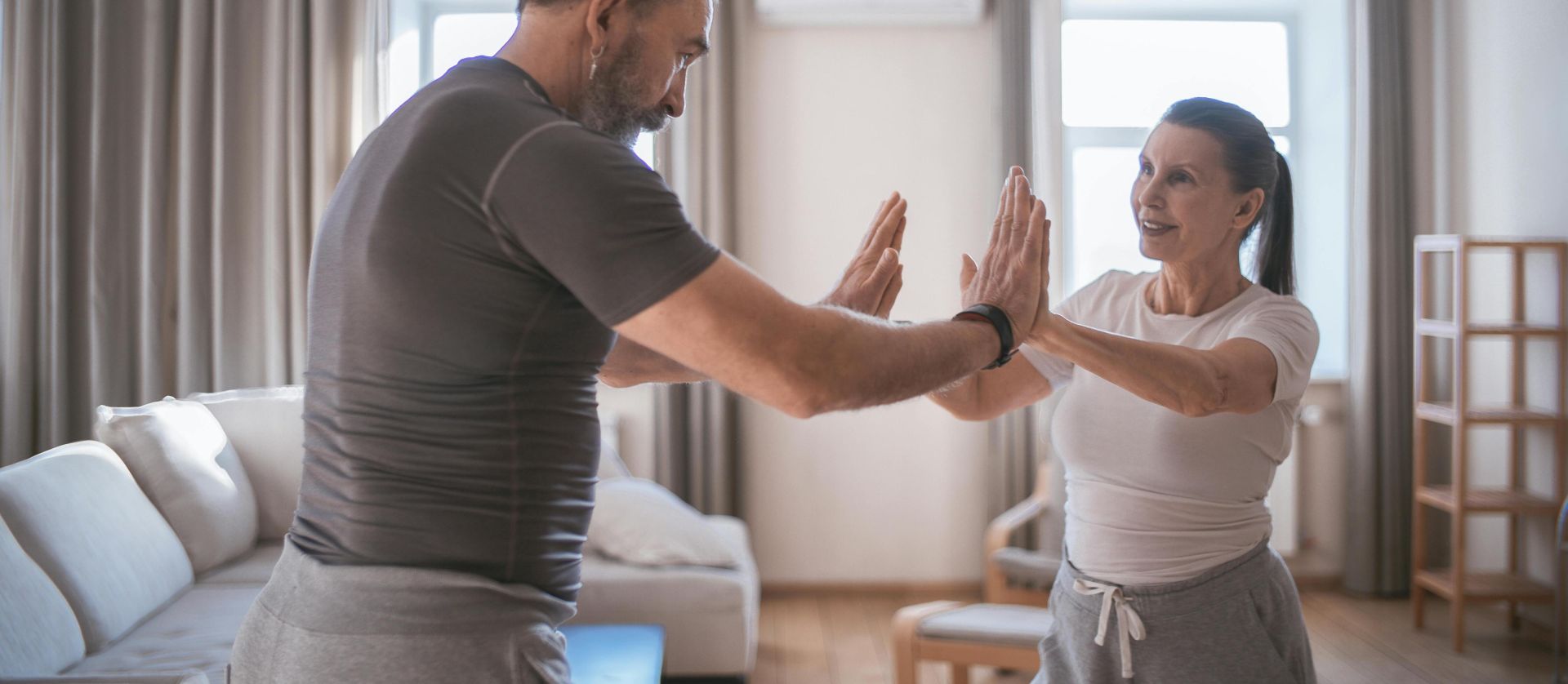Elderly couple practicing joint exercises indoors, promoting health and fitness.
